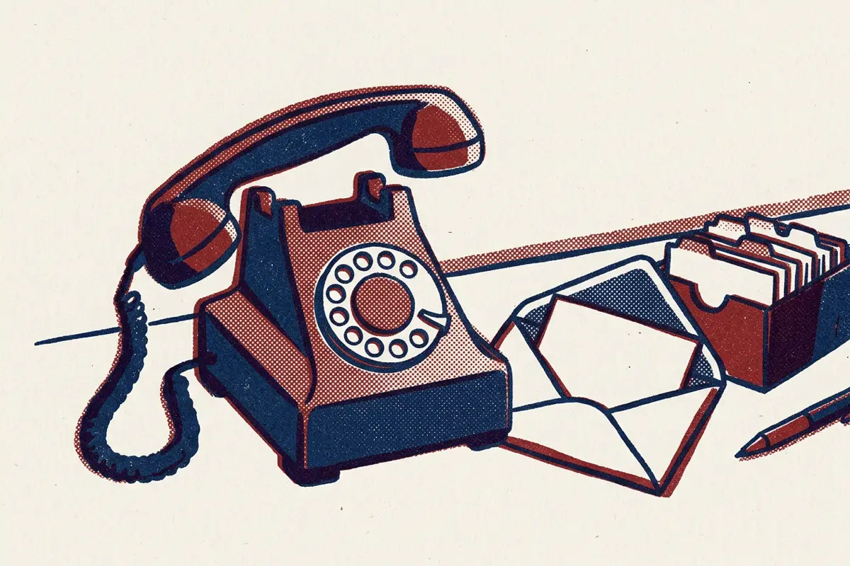 A rotary telephone with its handset lifted, beside an open envelope and a card index box.